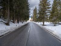 an empty road surrounded by snow and trees in the winter time, near a mountain