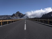 a highway in front of a mountain with clouds in the sky and fog in the distance