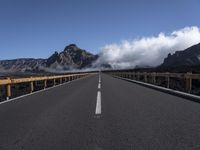 a highway in front of a mountain with clouds in the sky and fog in the distance