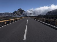 a highway in front of a mountain with clouds in the sky and fog in the distance