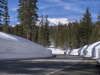 a long straight road in the woods next to a snowy hill, in front of trees, with a snowbank