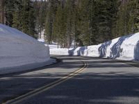a long straight road in the woods next to a snowy hill, in front of trees, with a snowbank