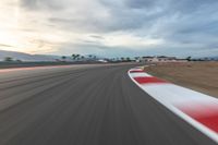 a photo of a dirt race track with sun setting in the distance of the track