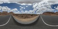 a view of an empty desert with a road going through it with a man on a motorcycle riding along one