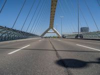 a truck driving across a bridge near a street corner near buildings and a bridge with many cables