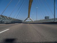 a truck driving across a bridge near a street corner near buildings and a bridge with many cables