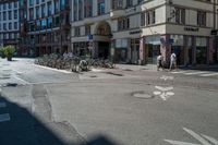 an empty street with parked bikes in the foreground and a tall building and a couple people walking across it