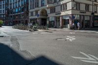 an empty street with parked bikes in the foreground and a tall building and a couple people walking across it