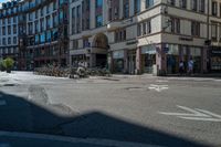 an empty street with parked bikes in the foreground and a tall building and a couple people walking across it