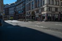 a city street with a building and multiple buildings in the background is blue sky with sun shining down