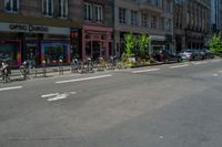 bicycles are parked in the corner by the curb and buildings on the other side of the road