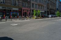 bicycles are parked in the corner by the curb and buildings on the other side of the road