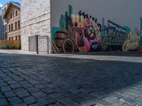 street view with brick buildings and an outdoor bench near wall, in large area with colorful street art