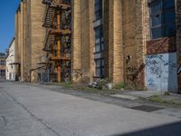 a yellow fire hydrant stands in the center of an empty alley way with a building and stairs in the back