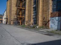 a yellow fire hydrant stands in the center of an empty alley way with a building and stairs in the back