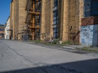 a yellow fire hydrant stands in the center of an empty alley way with a building and stairs in the back