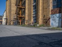 a yellow fire hydrant stands in the center of an empty alley way with a building and stairs in the back