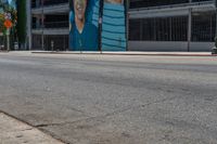 a man wearing a wet suit crossing an intersection with his skateboard on the sidewalk