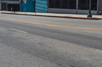 a man wearing a wet suit crossing an intersection with his skateboard on the sidewalk