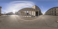 a fish eye lens of a street with a building and sun in the background with cars