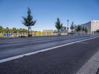 a picture of a city street and some buildings in the background of this photo and trees near an asphalt roadway