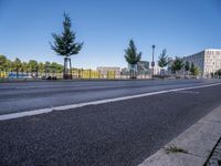 a picture of a city street and some buildings in the background of this photo and trees near an asphalt roadway