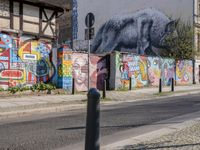 a wall of street graffiti and a street corner with people walking past it and another building in the back ground