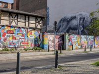 a wall of street graffiti and a street corner with people walking past it and another building in the back ground