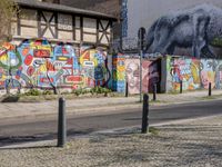 a wall of street graffiti and a street corner with people walking past it and another building in the back ground