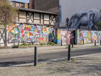 a wall of street graffiti and a street corner with people walking past it and another building in the back ground