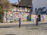 a wall of street graffiti and a street corner with people walking past it and another building in the back ground