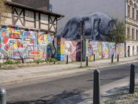 a wall of street graffiti and a street corner with people walking past it and another building in the back ground