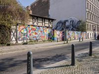 a wall of street graffiti and a street corner with people walking past it and another building in the back ground