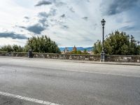 a street with a few cars parked near it on a cloudy day next to a stone wall