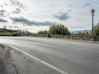 a street with a few cars parked near it on a cloudy day next to a stone wall