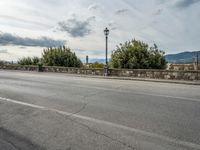 a street with a few cars parked near it on a cloudy day next to a stone wall