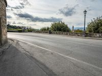 a street with a few cars parked near it on a cloudy day next to a stone wall