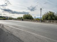 a street with a few cars parked near it on a cloudy day next to a stone wall