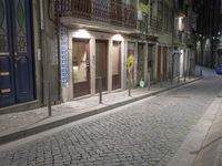 an empty sidewalk with stone pavement and buildings at night in the dark, with two bikes parked on both sides