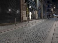 an empty sidewalk with stone pavement and buildings at night in the dark, with two bikes parked on both sides