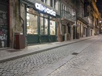 an empty sidewalk with stone pavement and buildings at night in the dark, with two bikes parked on both sides