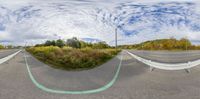 a street and a road next to each other under a cloudy blue sky as a fish eye lens