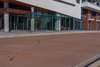 street signs stand out on the empty sidewalk in front of a large building with glass doors