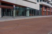 street signs stand out on the empty sidewalk in front of a large building with glass doors