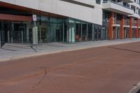 street signs stand out on the empty sidewalk in front of a large building with glass doors