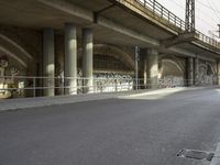 a person riding a skateboard down a street next to a bridge with graffiti on it