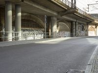 a person riding a skateboard down a street next to a bridge with graffiti on it