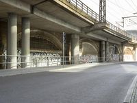 a person riding a skateboard down a street next to a bridge with graffiti on it