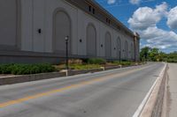 a picture of an empty street that is by some buildings in the distance with trees and bushes in front