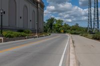 a picture of an empty street that is by some buildings in the distance with trees and bushes in front